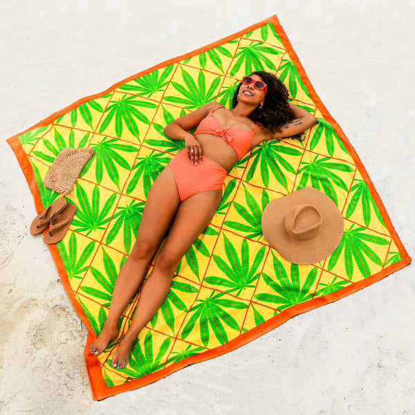 Luxurious big beach towel with bright colors and green bud leaves. Girl laying on oversized towel at the beach.